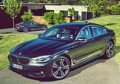 a black car parked on the side of a road in front of some trees and grass