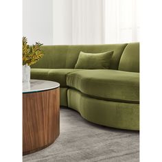 a living room with a large green sectional couch and round coffee table in front of it