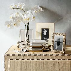 there is a vase with flowers and pictures on the table next to it, along with two framed photographs