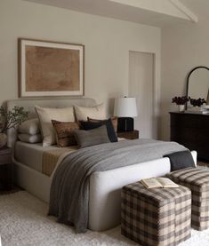 a bedroom with a large bed and two stools in front of the bed, along with a painting on the wall