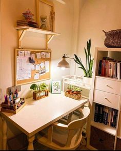 a white desk topped with lots of books and plants next to a wall mounted book shelf