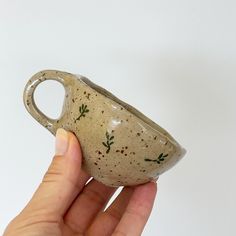 a hand holding a small ceramic cup with green sprinkles on it's side