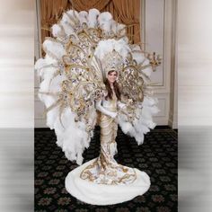 a woman dressed in white and gold with a large feathered fan on her head