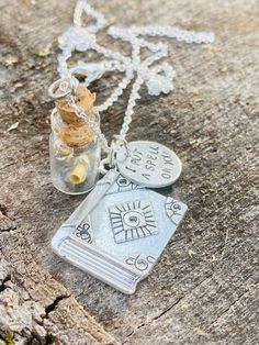 a necklace with two charms on it sitting on top of a wooden table next to a bottle