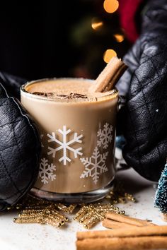 a cup of hot chocolate with cinnamon sticks in it next to some christmas decorations and black gloves