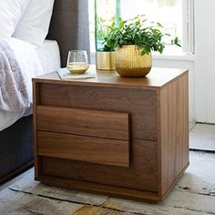 a nightstand with a potted plant on top of it next to a glass of wine