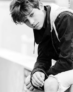 a young man sitting on top of a wooden bench next to a wall with his hand on his knee