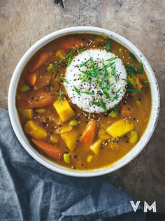 a white bowl filled with stew and rice on top of a wooden table next to a napkin