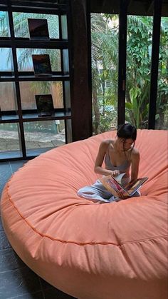 a woman sitting on an orange bean bag chair reading a book in the living room