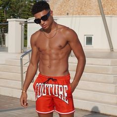 a shirtless young man wearing red shorts and sunglasses