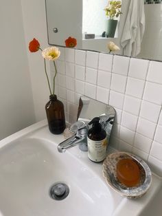 a bathroom sink with soap, lotion and flowers in the vase on it's side