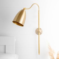 a gold wall light next to a bed in a room with white walls and pillows