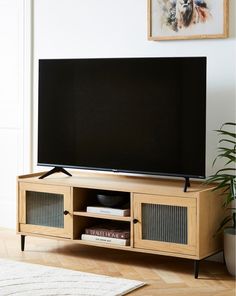 a flat screen tv sitting on top of a wooden entertainment center next to a potted plant