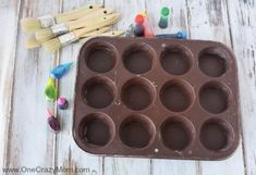 an ice cream tray filled with chocolate cups next to paintbrushes and wooden pegs