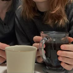 two people are sitting at a table with coffee in front of them and one is holding a mug