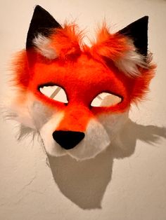 a red fox mask with black ears and orange fur on it's head is hanging from the wall