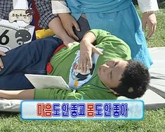 a man laying on top of a grass covered field next to people holding an electronic device