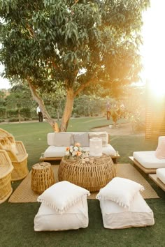 an outdoor seating area with wicker furniture and pillows on the grass in front of a tree