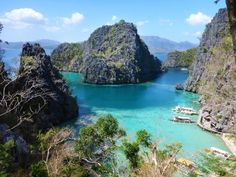 boats are docked in the clear blue water near large rocks and cliffs on an island