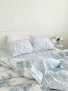 an unmade bed with blue and white comforter on it's side table