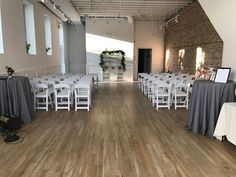 a room filled with white chairs and tables covered in gray tablecloths on top of hard wood flooring