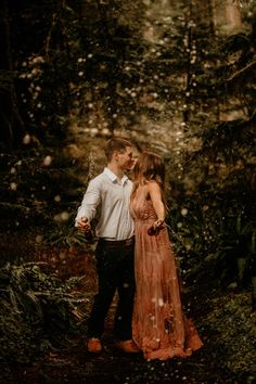 a man and woman are standing in the woods with snow falling all over their faces