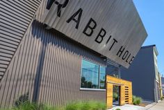 the entrance to rabbit hole in an industrial building with grass growing on the sidewalk and large metal letters above it