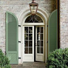 a white door with green shutters and a lantern