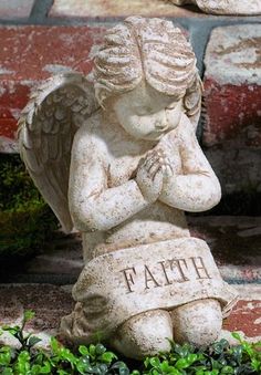 a statue of an angel sitting on the ground with his hands clasped to his chest