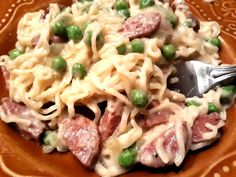 a plate full of pasta with peas and ham on it, next to a fork