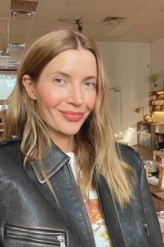 a woman wearing a black leather jacket and smiling at the camera in front of shelves