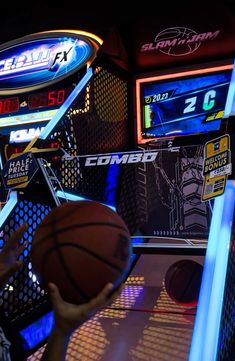 a person is holding a basketball in front of several televisions and neon signs on the wall