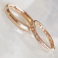 two gold wedding rings with pink and white diamonds on the inside of each ring, set against a light background