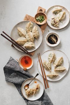 dumplings are served on plates with chopsticks and sauce