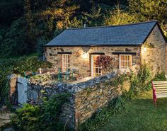 an old stone house with a garden in the foreground and a wooden bench to the side