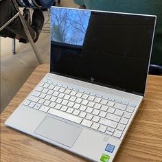 an open laptop computer sitting on top of a wooden table next to a person's feet