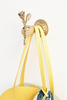 a yellow purse hanging from a hook on a white wall next to a round bag