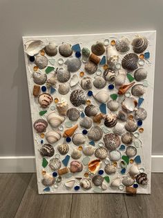 a painting made out of seashells and sea glass on a wooden floor next to a wall