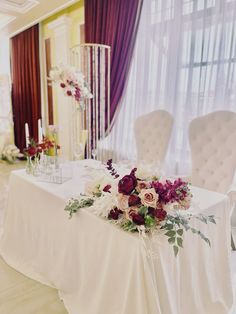 the table is set up with white chairs and flowers on it, along with candles