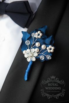 a boutonniere is adorned with pearls and blue satin flowers on a black suit lapel