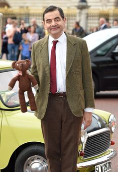 a man in a suit and tie holding a teddy bear next to a yellow car