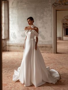 a woman in a white wedding dress standing on the floor with her hand on her shoulder