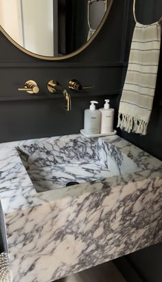 a bathroom sink with marble counter top and gold faucet, in front of a mirror