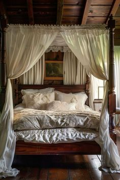 a canopy bed with white drapes and pillows in a room that has wooden floors