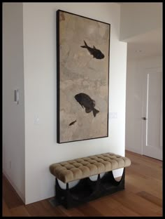 a painting hanging on the wall above a bench in a room with hardwood floors and white walls