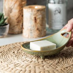 a hand is picking up a piece of soap from a green bowl on a woven place mat