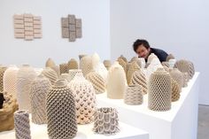 a man is looking at several vases on display in a room with white walls