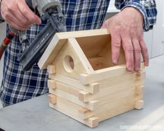 a man holding a hammer next to a small wooden house made out of wood planks