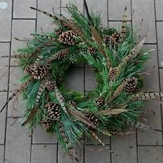 a christmas wreath with pine cones and needles on the side of a brick road,