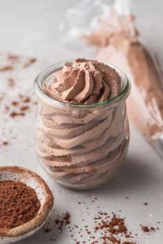 a glass jar filled with chocolate frosting next to a scoop of powdered cocoa